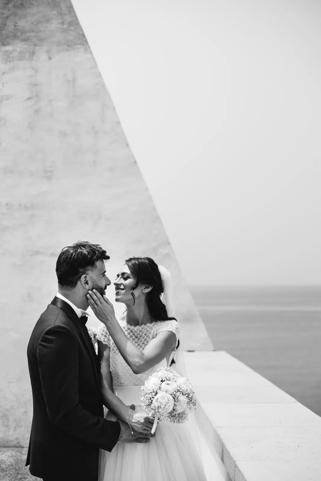 Gli sposi davanti a un muro bianco sul mare, in bianco e nero
