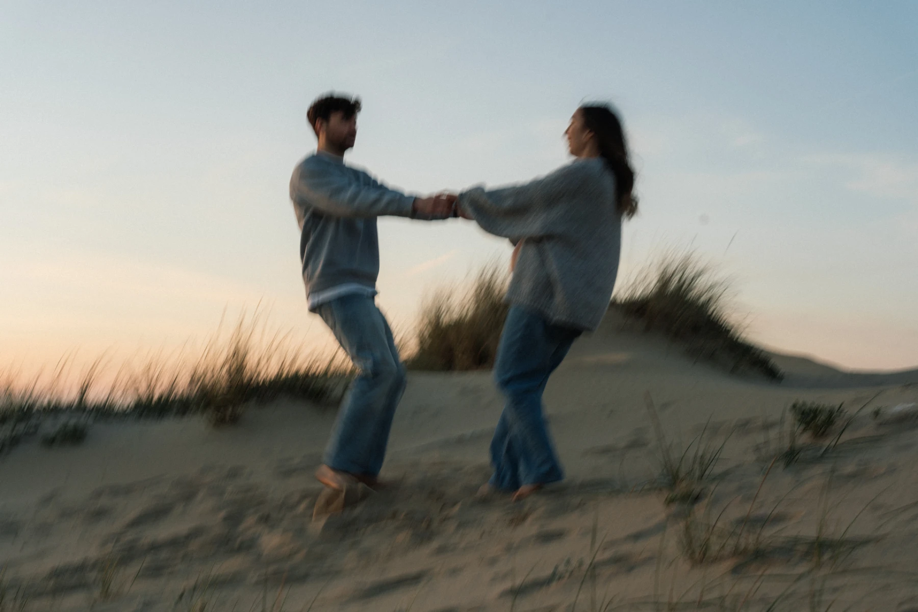 Una coppia gira tenendosi per mano sulle dune al tramonto
