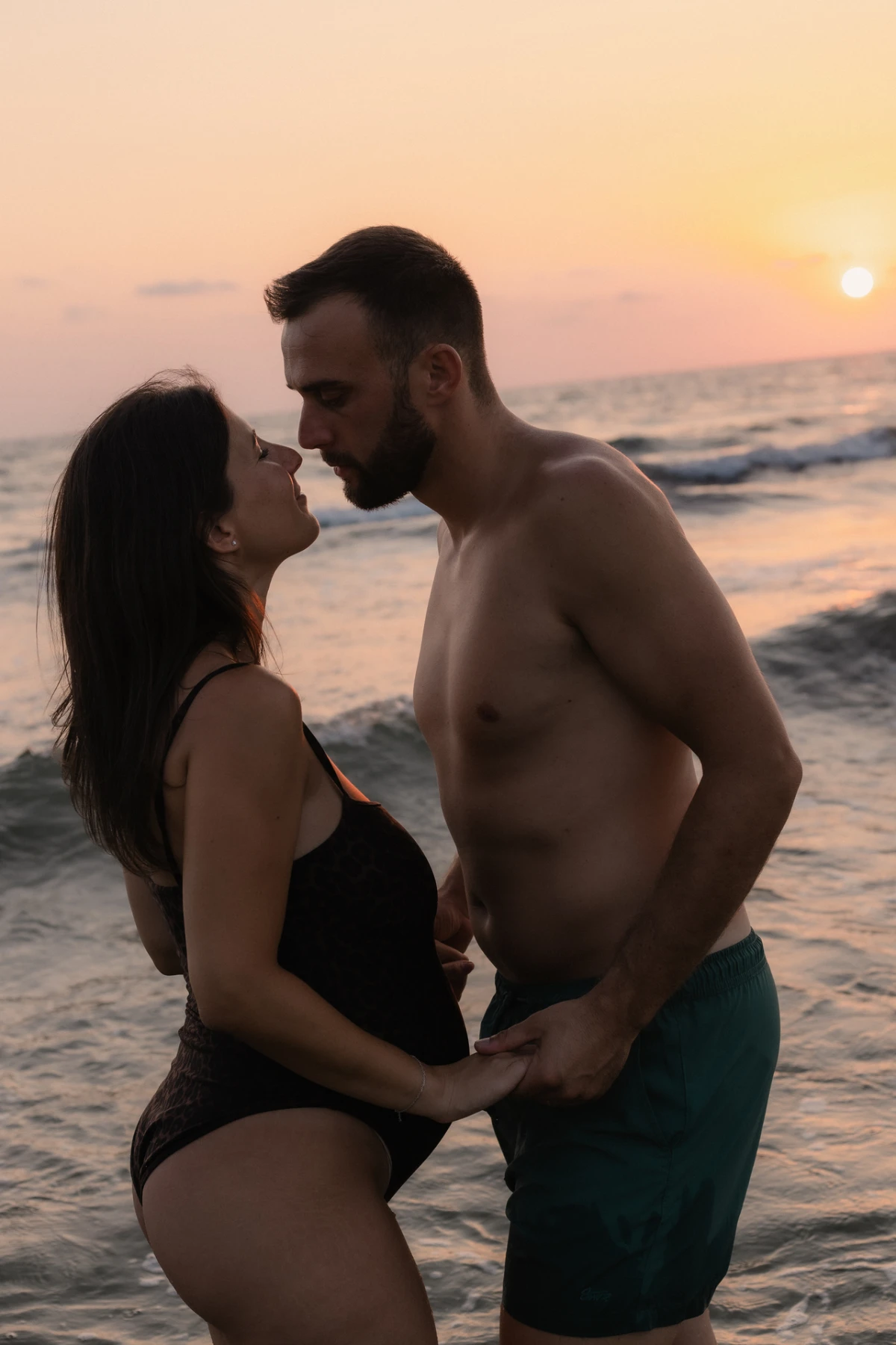 Una coppia in attesa si sfiora il naso tra le onde al tramonto