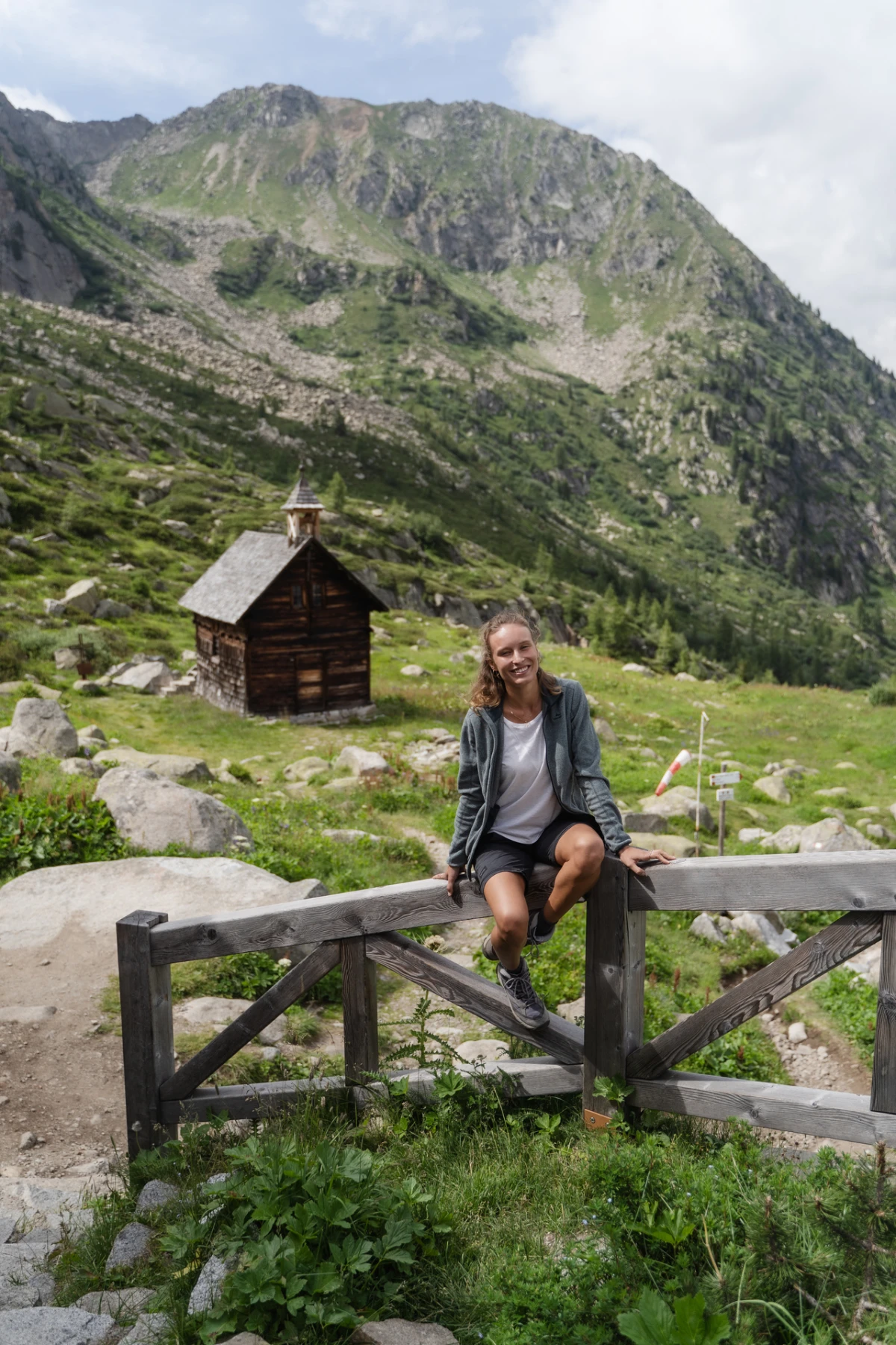 Olly seduta su una staccionata in montagna, con una baita di legno alle spalle