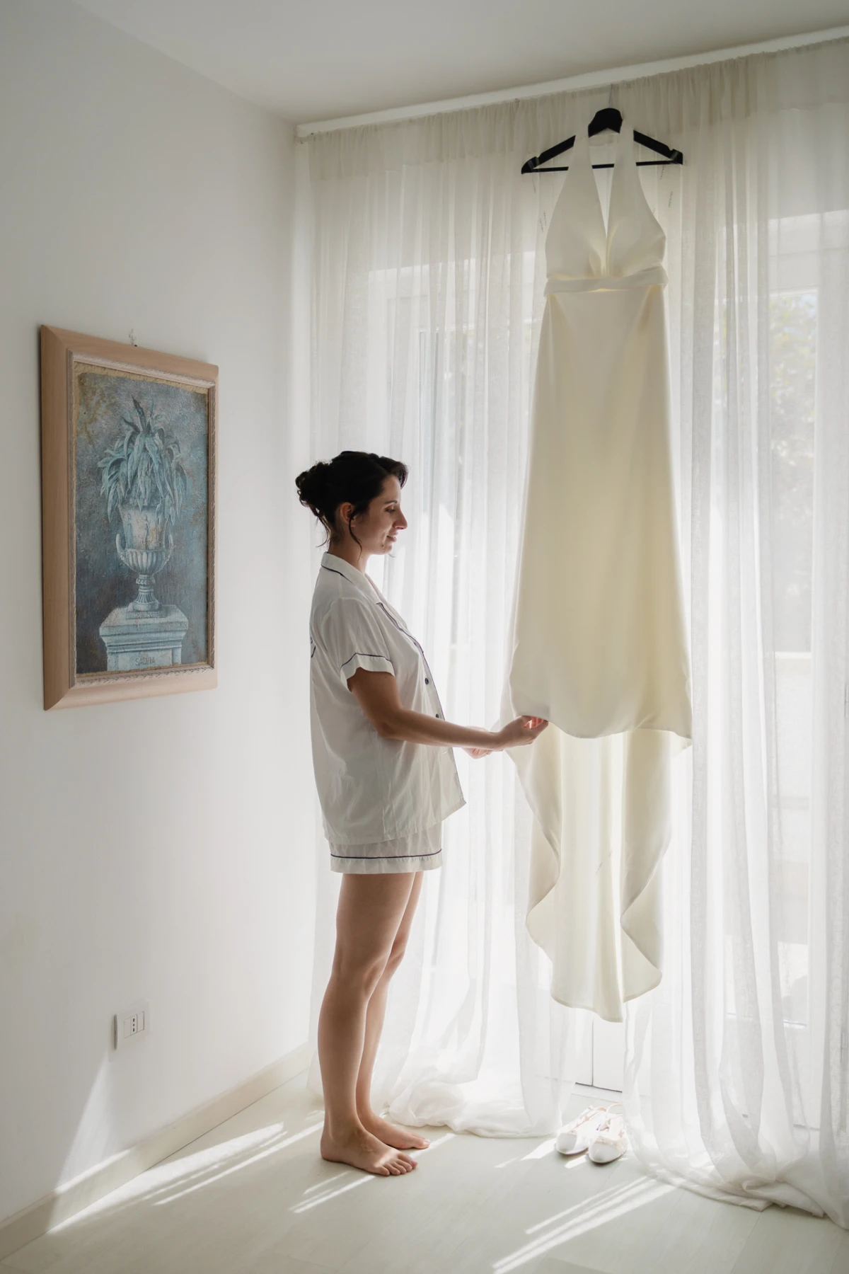 La sposa in pigiama tocca l'abito appeso alla finestra