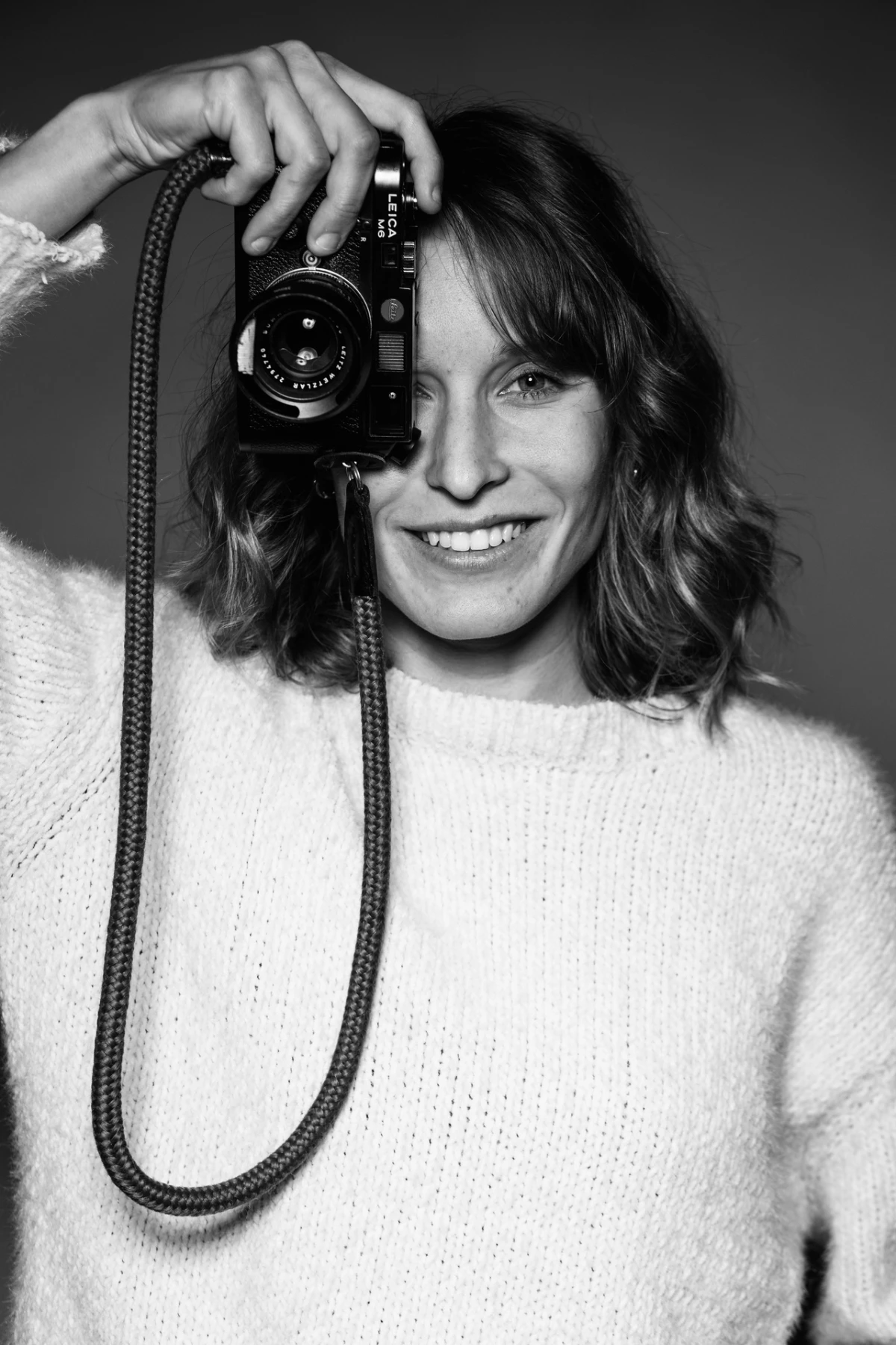 Olly sorride con la macchina fotografica davanti a un occhio, in bianco e nero