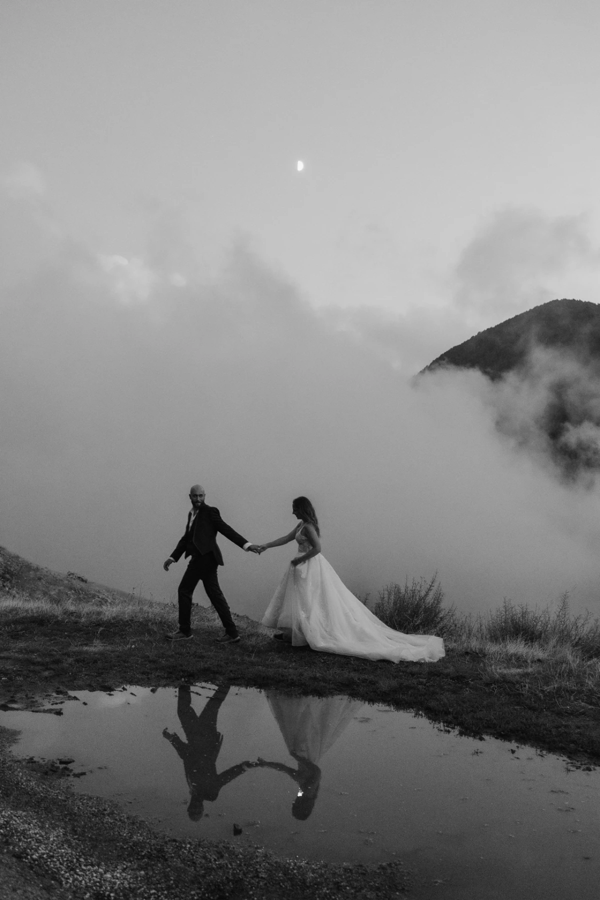 Gli sposi riflessi in una pozza tra la nebbia, in bianco e nero